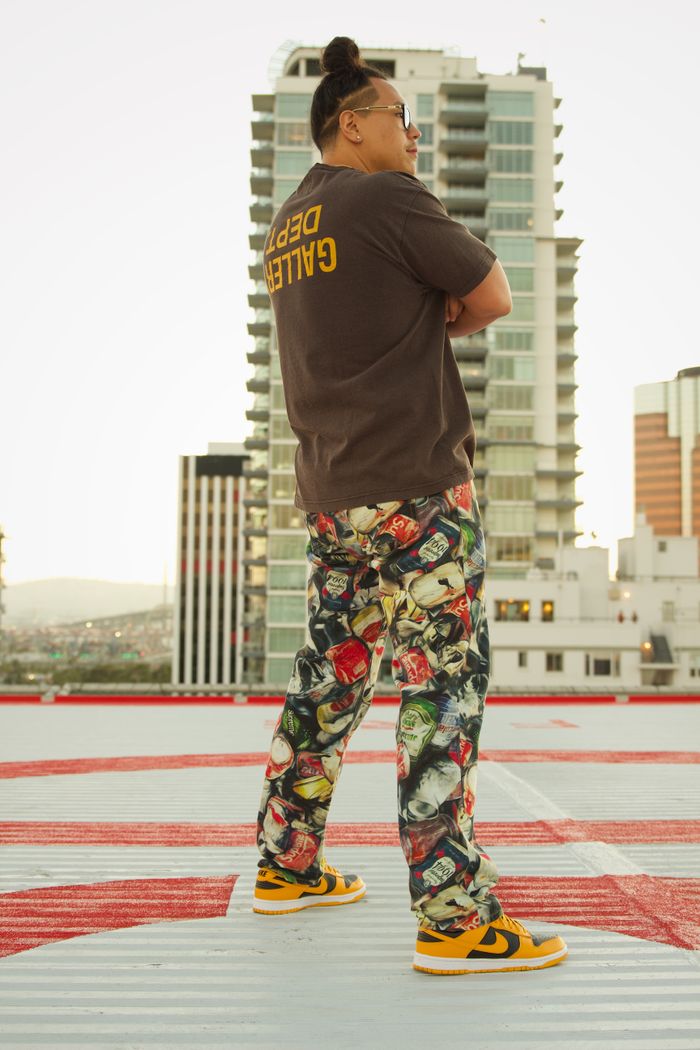 Stylish man poses on a rooftop in Los Angeles, showcasing urban fashion with a vibrant cityscape backdrop.