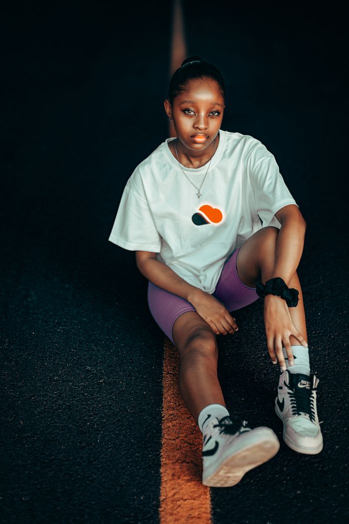 Casual and stylish young woman sitting on a street in urban fashion attire.