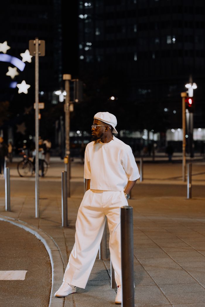 Fashionable man in white outfit standing on city street at night.