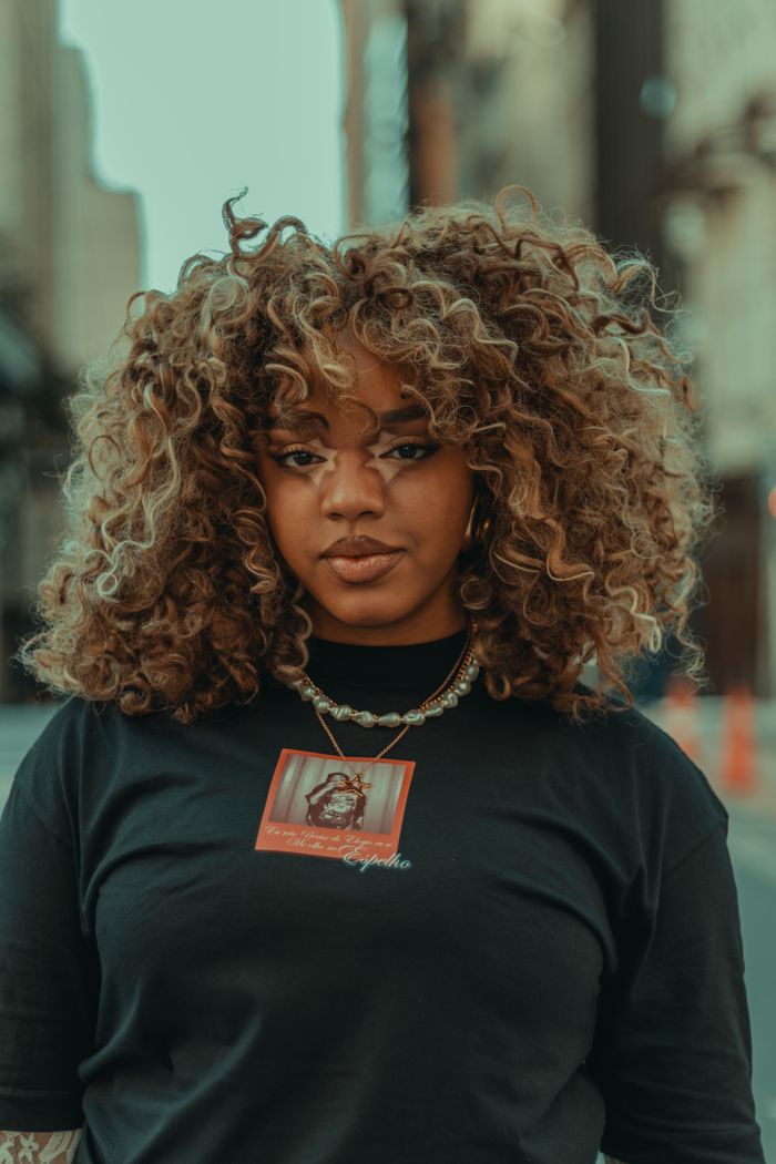 Portrait of a fashionable woman with curly hair wearing a black shirt in an urban environment.